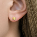 A close-up of a woman's ear wearing an 18K yellow gold flower stud earring designed by Laura Pearce.