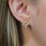 A close-up of a woman's ear wearing an 18K yellow gold stud earring with four clear diamonds in a quad design cluster.