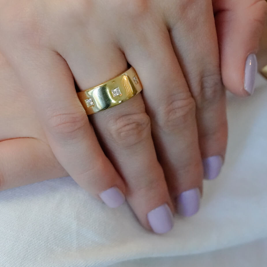 18K Gold ring on a finger with light purple nail polish on a white background
