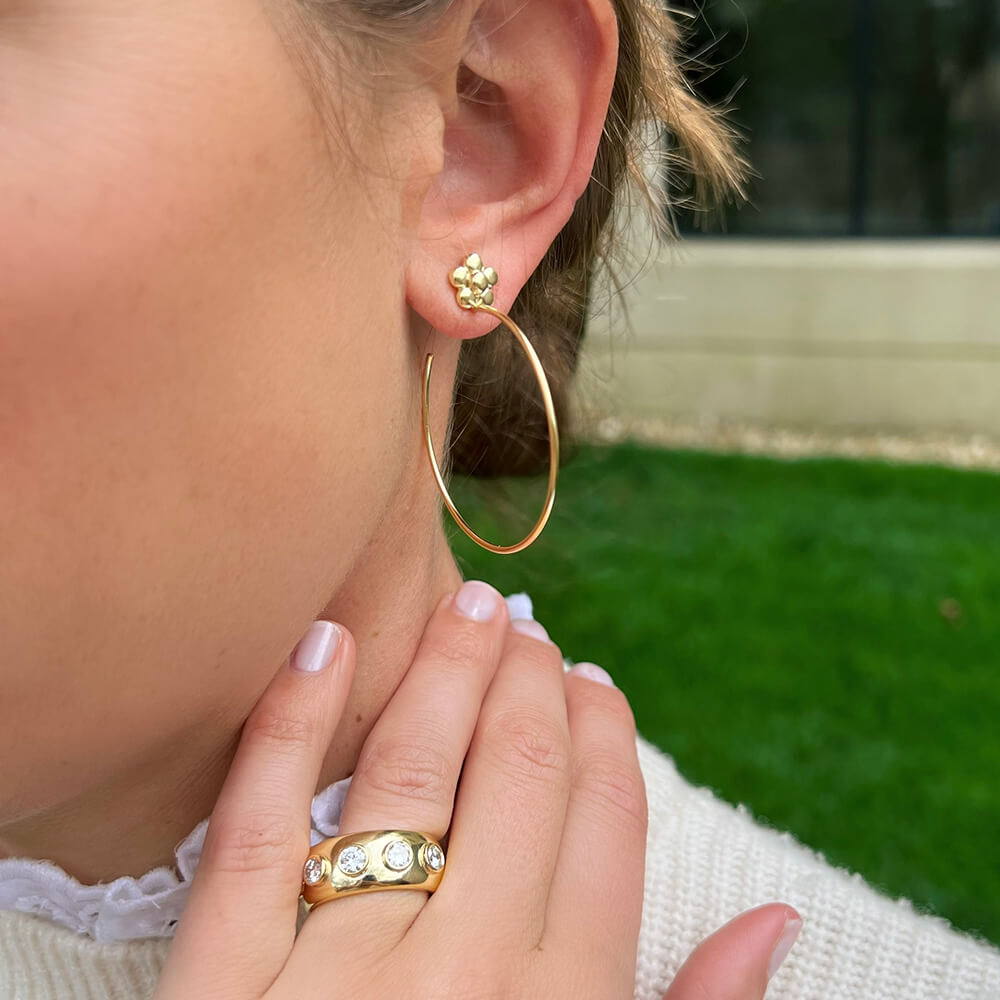 Close-up of a woman wearing 18K gold hoop earrings and rings 