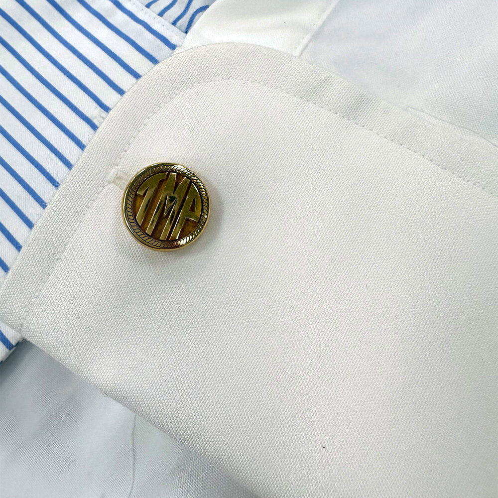 Close-up of a monogrammed cufflink with initials on a white shirt sleeve.