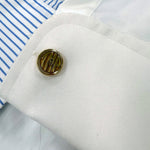 Close-up of a monogrammed cufflink with initials on a white shirt sleeve.