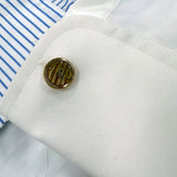 Close-up of a monogrammed cufflink with initials on a white shirt sleeve.