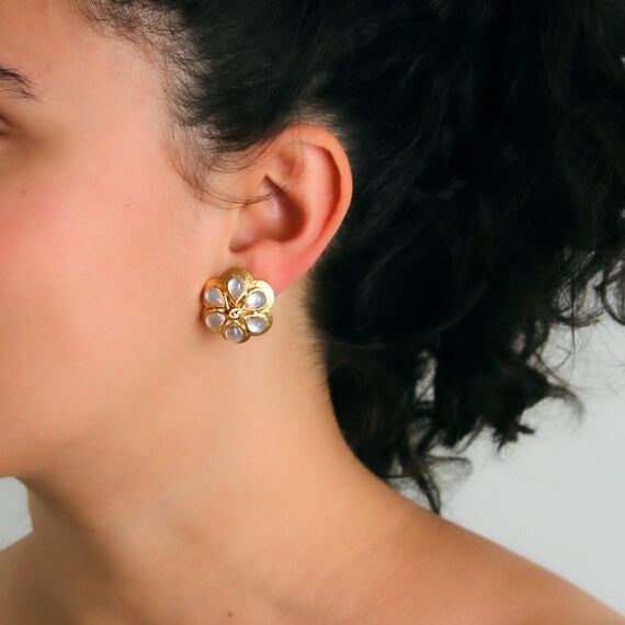 Close-up of a woman wearing a gold daisy-shaped earring with moonstones and diamonds