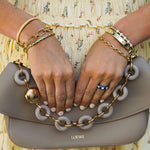 Woman holding a LOEWE handbag with gold chain detail, wearing multiple 18K gold bracelets and rings.