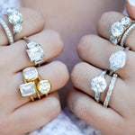 Close-up of hands wearing various diamond rings on a blurred background