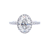 An oval-cut diamond engagement ring with a halo setting and a pavé band, shown on a solid white background.