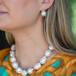 Close-up of a woman wearing a pearl necklace and earrings with a patterned top.
