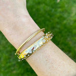 Gold bracelet with floral design on a wrist against a green background