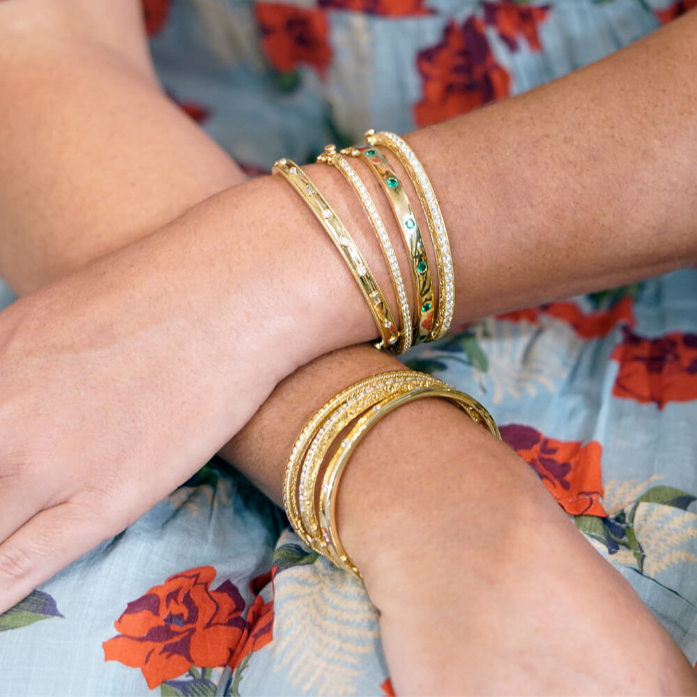 Gold bracelets on a wrist with a floral-patterned fabric background