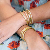 Gold bracelets on a wrist with a floral-patterned fabric background
