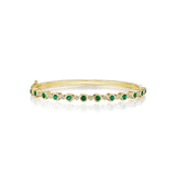 A yellow gold bangle bracelet with green emerald stones and diamond accents.