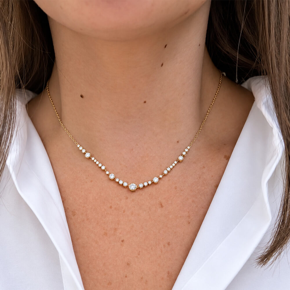 A delicate 18K yellow gold chain necklace with a curved row of diamonds and a central clear round diamond, shown worn on a model's neck over a white collared shirt.