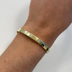 An 18K yellow gold bangle bracelet with small inset clear diamonds, shown worn on a woman's wrist against a plain light background.