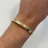An 18K yellow gold bangle bracelet with small inset clear diamonds, shown worn on a woman's wrist against a plain light background.