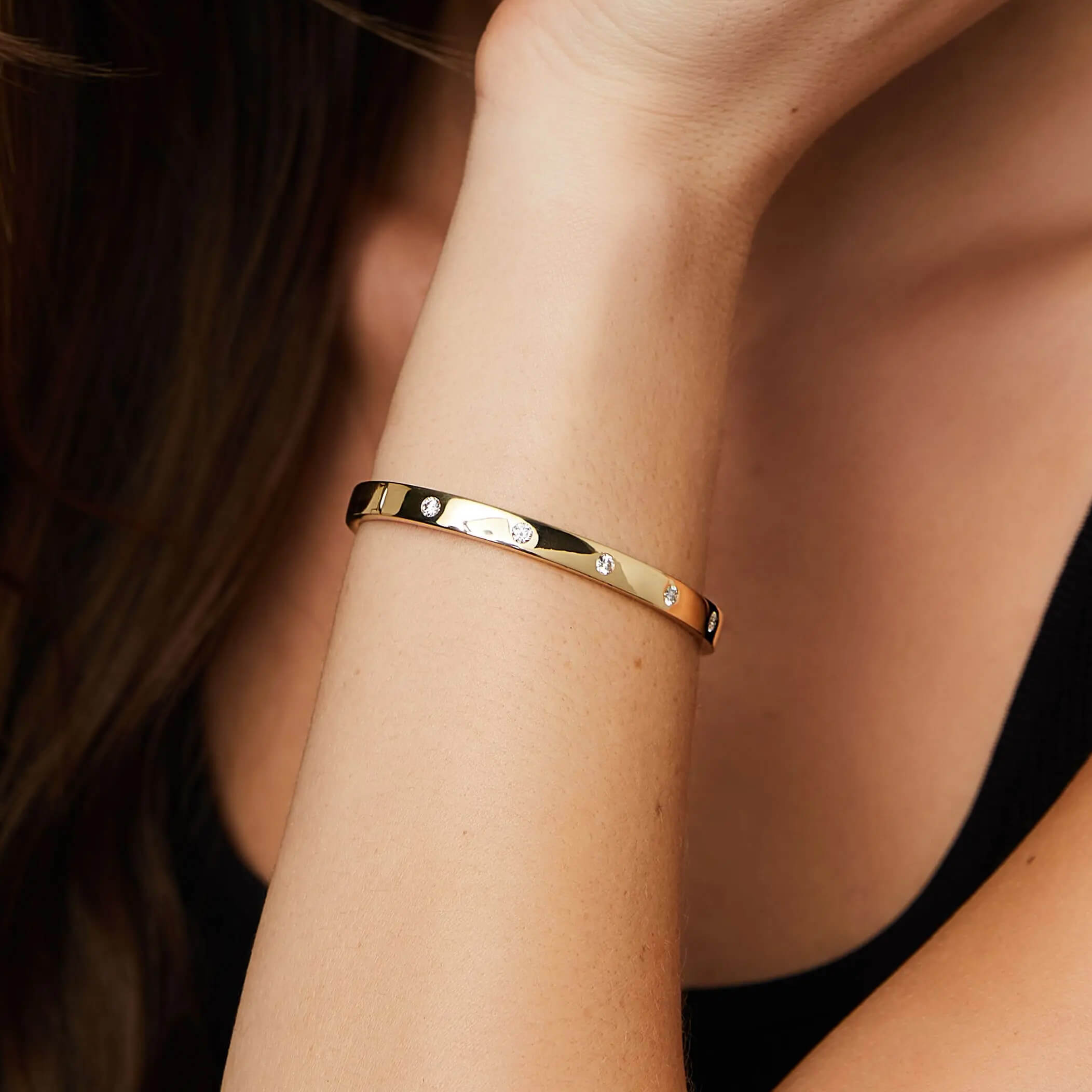 A slim gold bangle bracelet with small clear diamonds set along the band, worn on a woman's wrist.