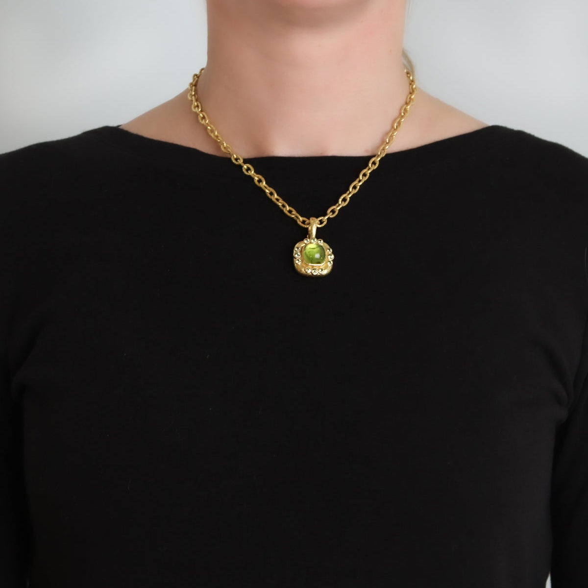 Woman wearing a gold chain necklace with a green Peridot pendant on a plain background