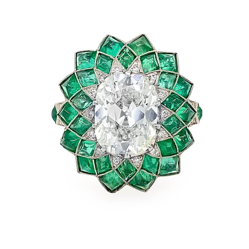 A vintage-style floral inspired ring featuring a large oval center diamond surrounded by a radiant halo of emeralds and small accent diamonds in platinum metal, set against a plain white background.