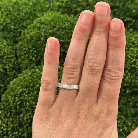 Hand wearing a platinum ring with 7 diamond stones totalling 1.65 carats against green blurred background