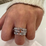 Close-up of a hand wearing three bezel set emerald cut diamond rings on a neutral background