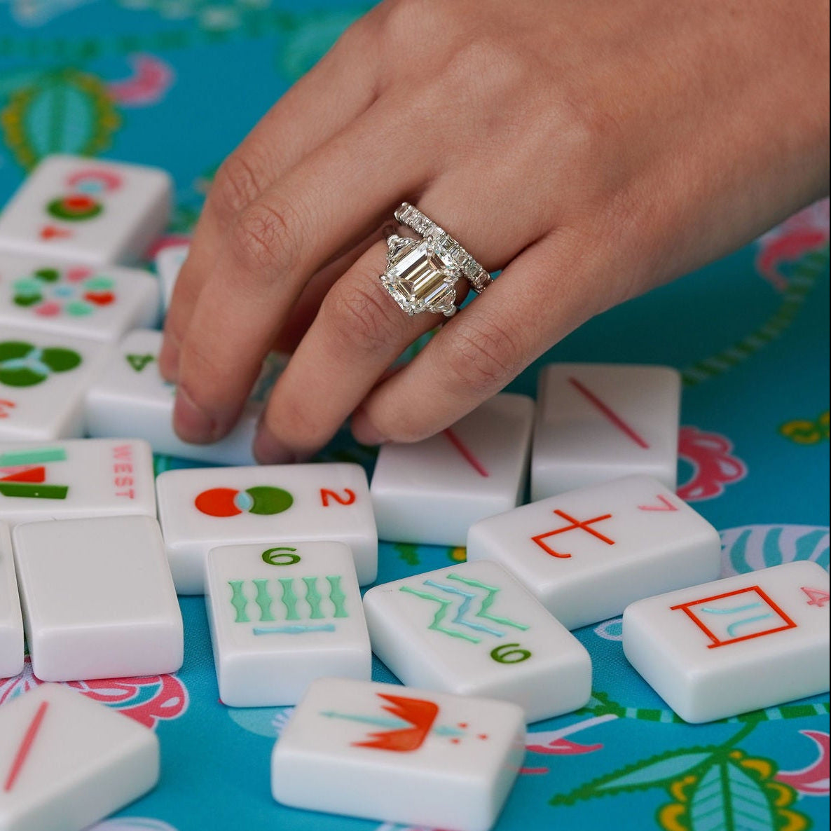 Woman's hand wearing Estate 5.4 carat Diamond ring playing with Mahjong tiles on a colorful board