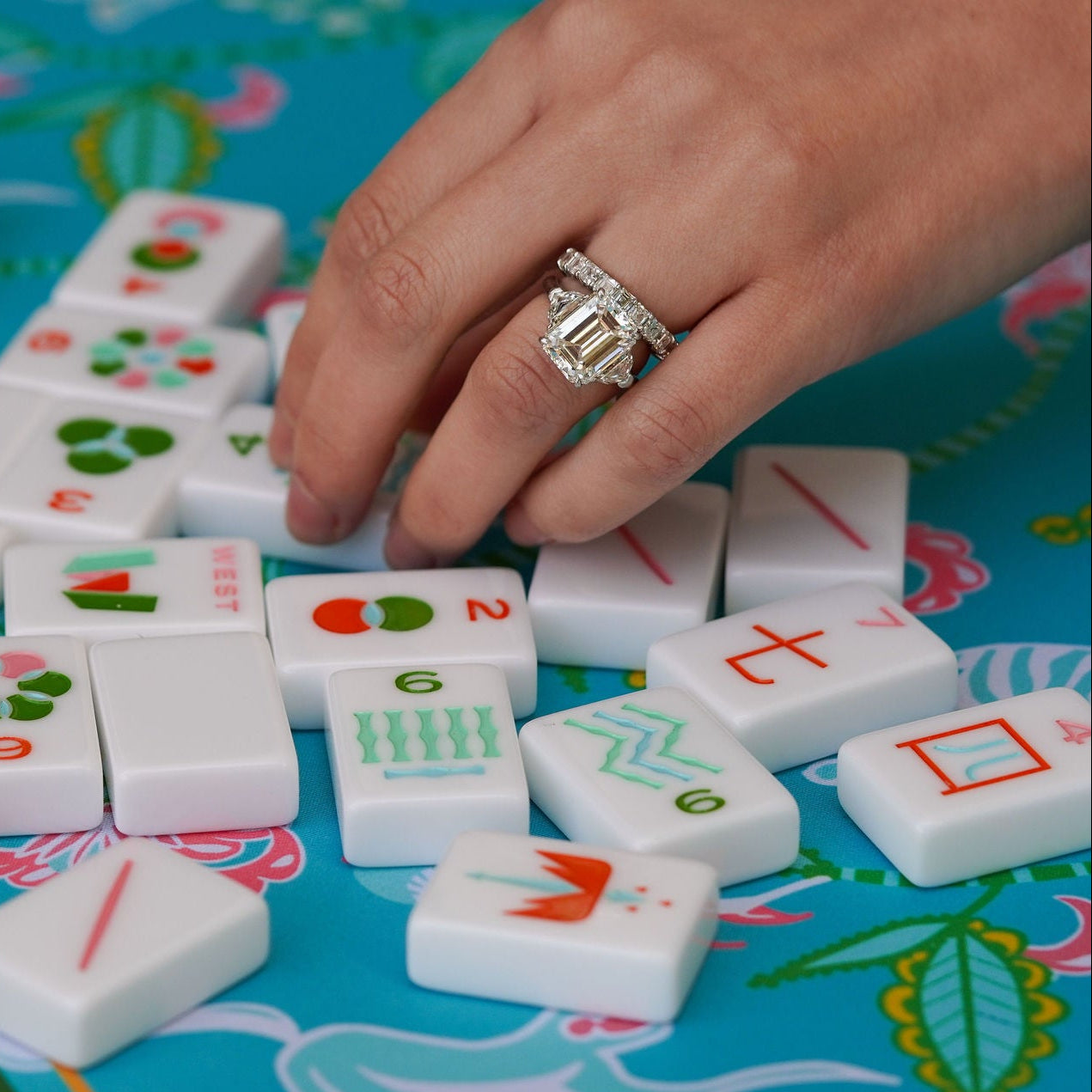 Woman's hand wearing Estate 5.4 carat Diamond ring playing with Mahjong tiles on a colorful board