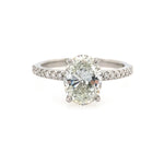 An oval-cut diamond solitaire engagement ring with a platinum band accented by pavé diamonds, shown on a plain white background.