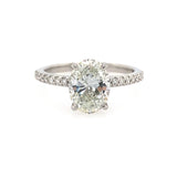 An oval-cut diamond solitaire engagement ring with a platinum band accented by pavé diamonds, shown on a plain white background.