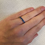 Hand wearing a ring with sapphire stones on a textured beige background