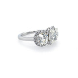 A platinum ring featuring three clear diamonds in halo settings, photographed on a clean white background.