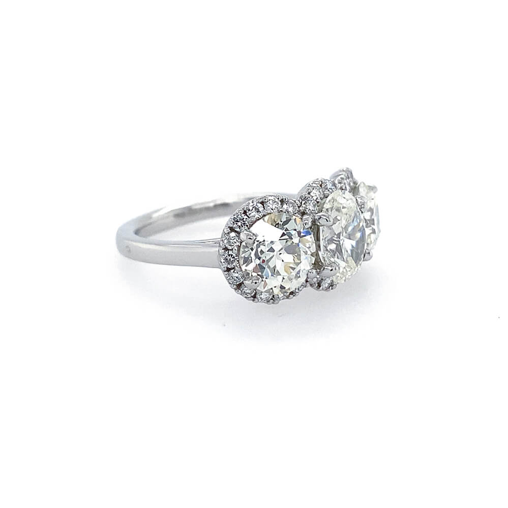 A platinum ring featuring three clear diamonds in halo settings, photographed on a clean white background.