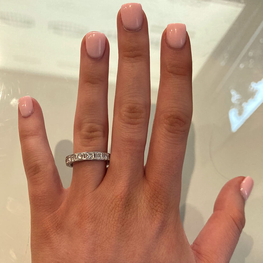 Hand wearing a platinum and diamond ring with pink nail polish on a neutral background