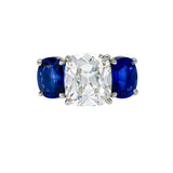 A ring with a platinum band and a cushion cut diamond in a setting with blue sapphires.
