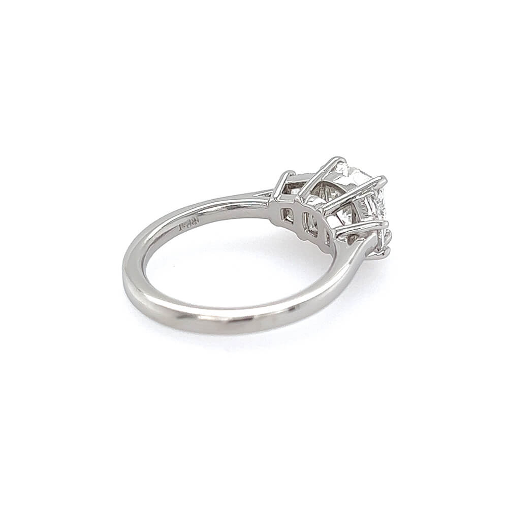 A platinum diamond ring with a cushion-cut center stone in a four-prong setting, shown from a side angle on a plain white background.