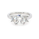 A three-stone diamond engagement ring with a round center diamond and trapezoid side diamonds on a polished platinum band, set against a plain white background.