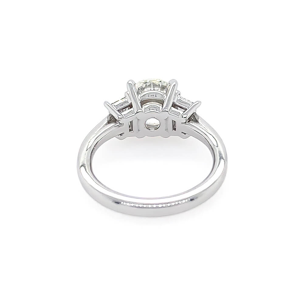 A platinum diamond ring with a round center stone and trapezoid side stones, shown from a inside view on a white background.