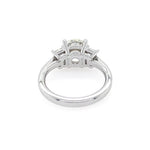 A platinum diamond ring with a round center stone and trapezoid side stones, shown from a inside view on a white background.