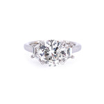 A custom-designed diamond engagement ring featuring a round center stone and two trapezoid side stones in a platimun metal setting, isolated on a white background.