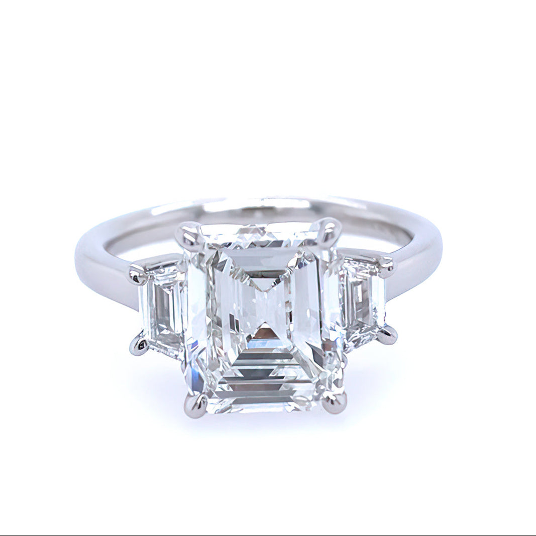 A platinum emerald cut diamond ring with trapezpoids on a white background