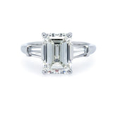 A platinum ring with an emerald cut center diamond and smaller baguette diamonds set in the band.