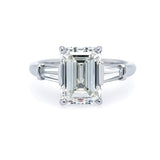 Custom platinum engagement ring with emerald-cut center diamond and baguette side dimaonds on a white background