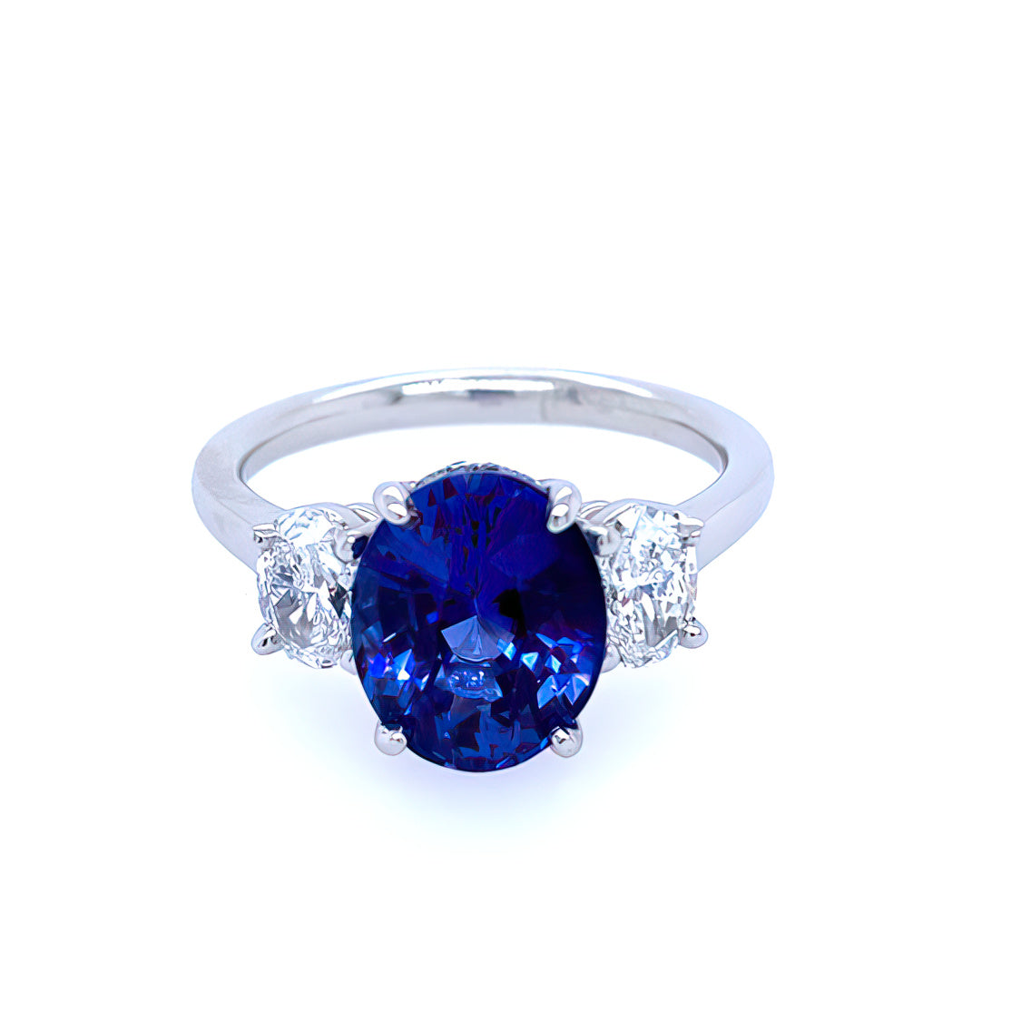 A custom designed platinum oval sapphire and diamond three stone ring with a large blue sapphire in the center and smaller diamonds on the sides.