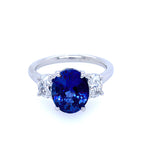 A custom designed platinum oval sapphire and diamond three stone ring with a large blue sapphire in the center and smaller diamonds on the sides.