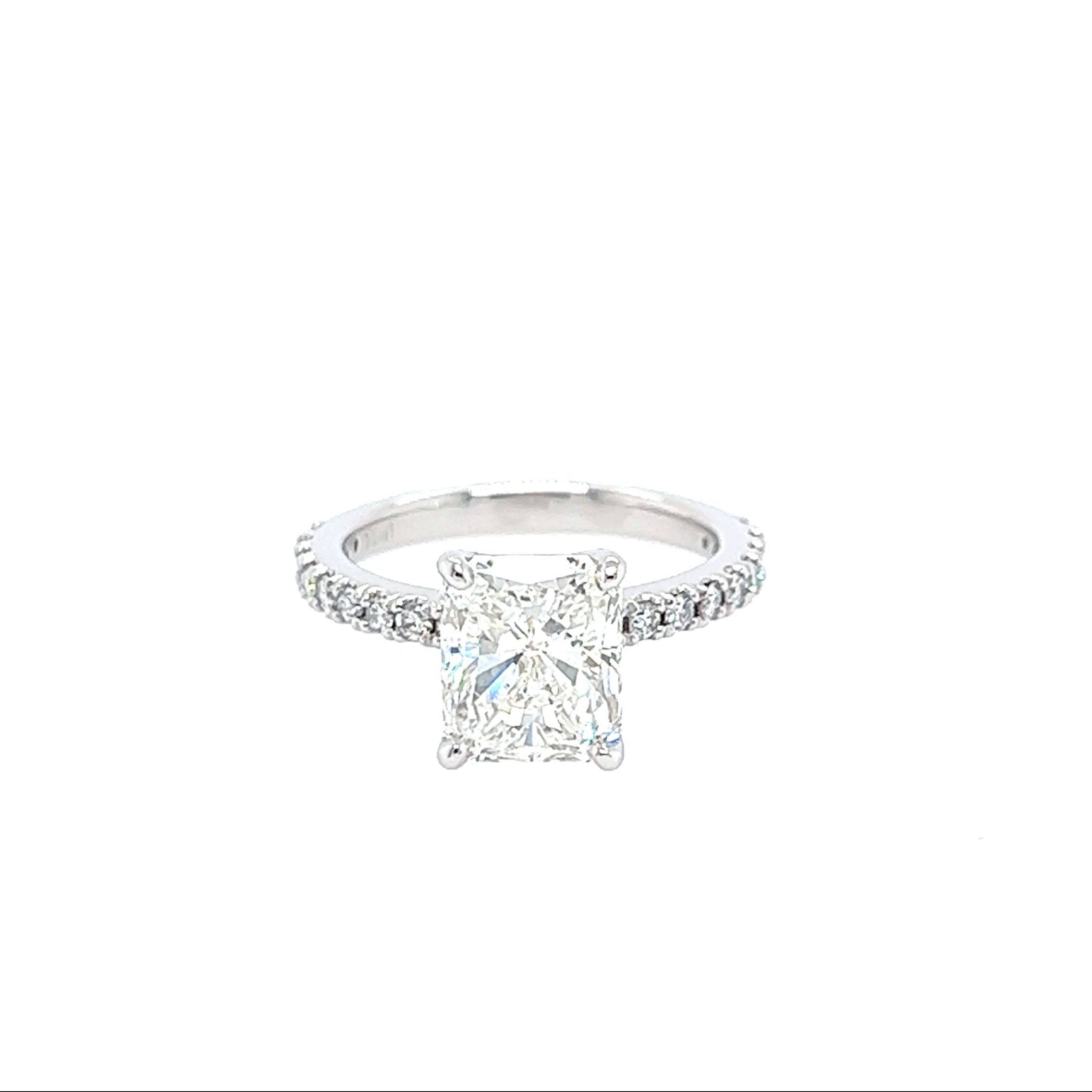 A Platinum and Diamond Radiant Cut Engagement Ring with a clear central diamond and smaller diamonds on the band, set against a white background.