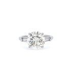 A platinum round brilliant diamond engagement ring with tapered baguette side stones.