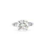 A platinum round brilliant diamond engagement ring with tapered baguette side stones.