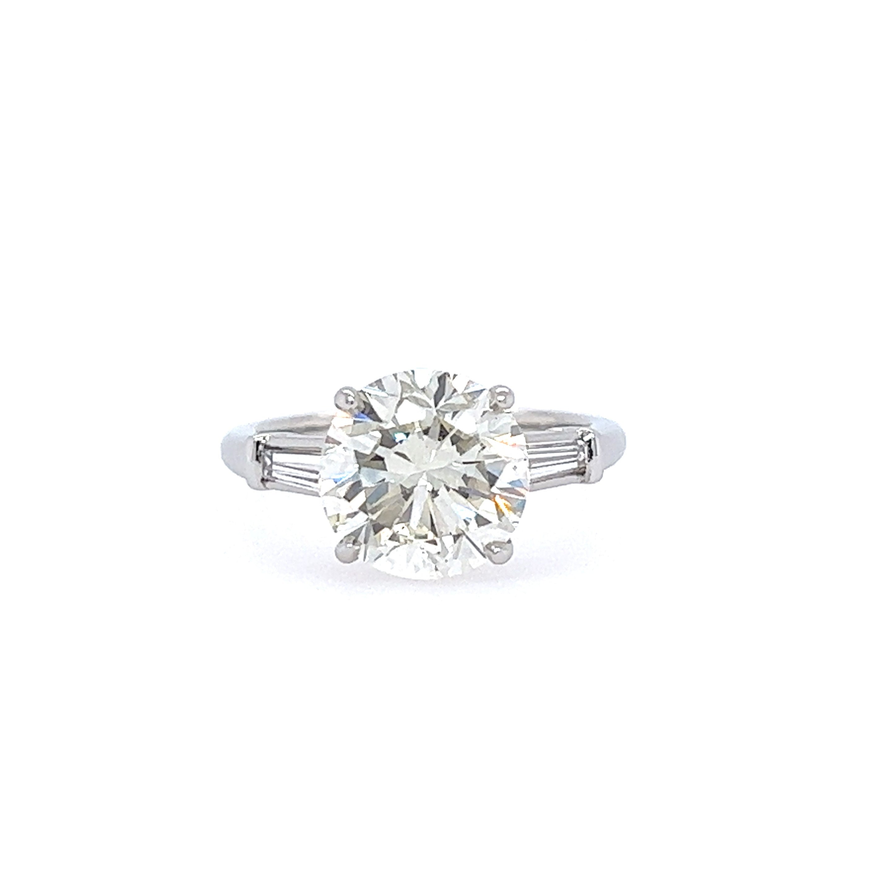 A platinum round brilliant diamond engagement ring with tapered baguette side stones.