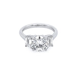 A platinum round diamond ring with emerald side stones set in a plain band