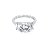 A platinum round diamond ring with emerald side stones set in a plain band