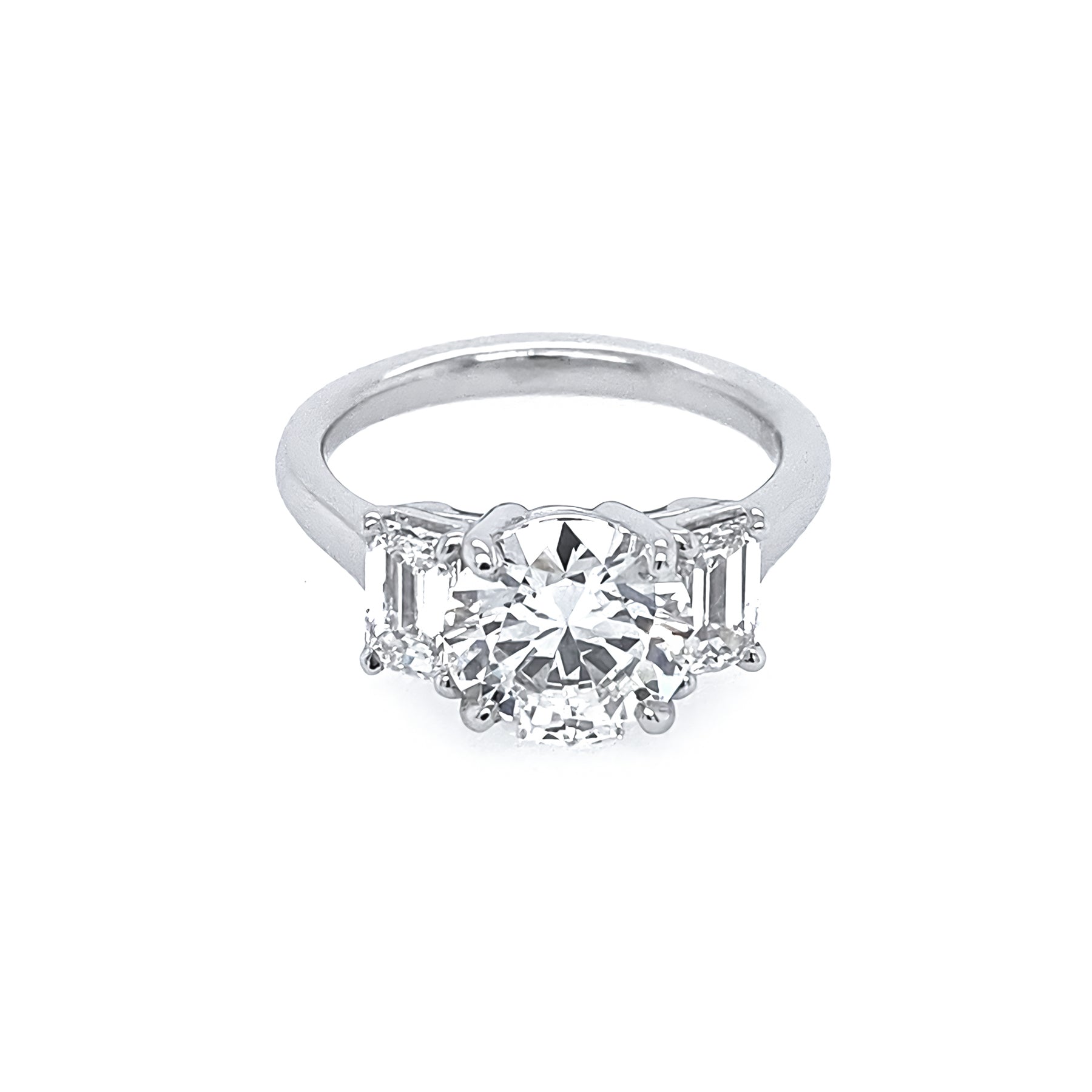 A platinum round diamond ring with emerald side stones set in a plain band